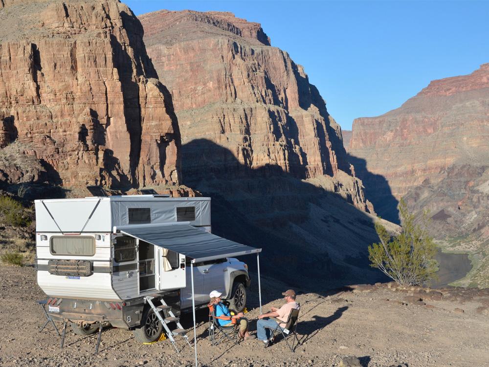 Two people sitting in the mountains next to a popup camper truck