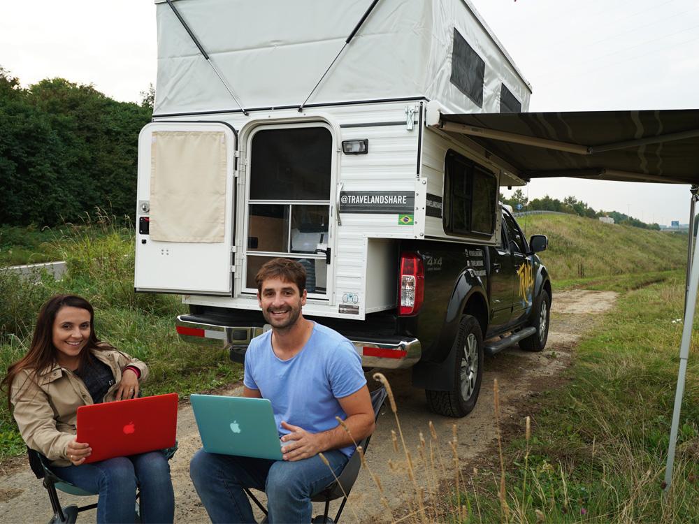 two people on laptops sitting in front of a pop up camper on track