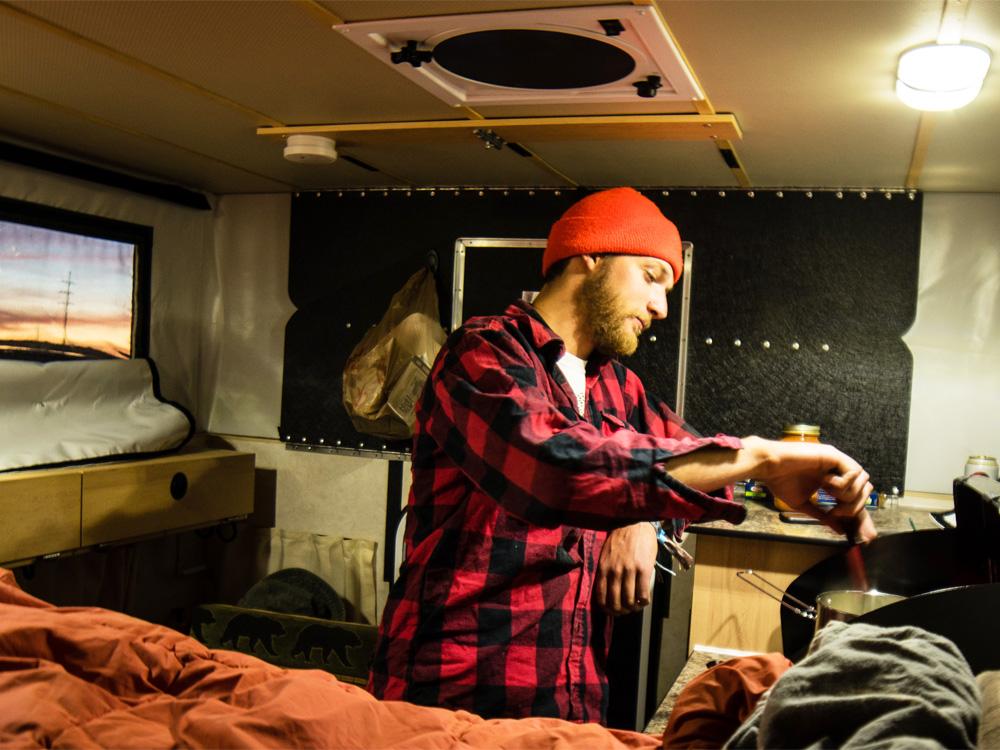 man cooking food inside a truck pop up camper