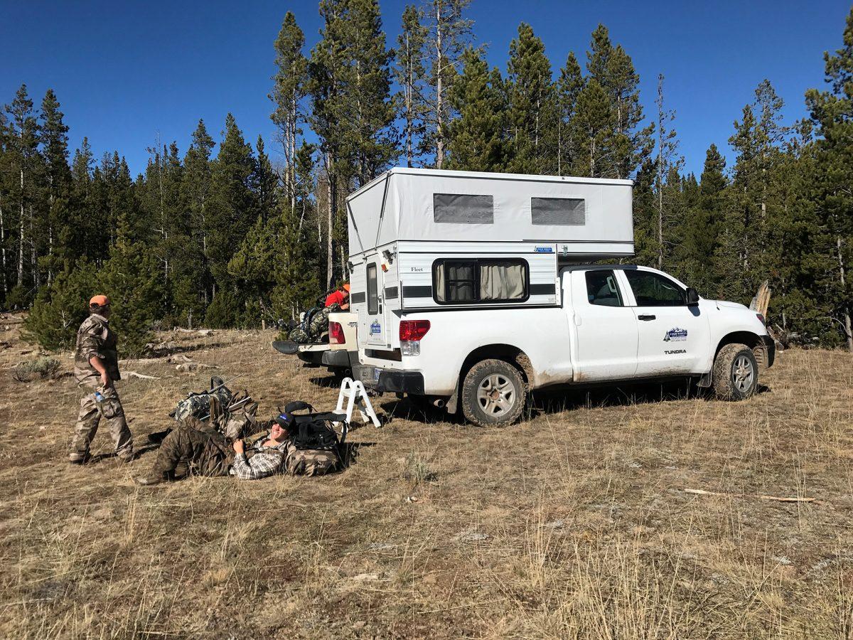 men sitting in the wilderness next to trucks with pop up camper beds