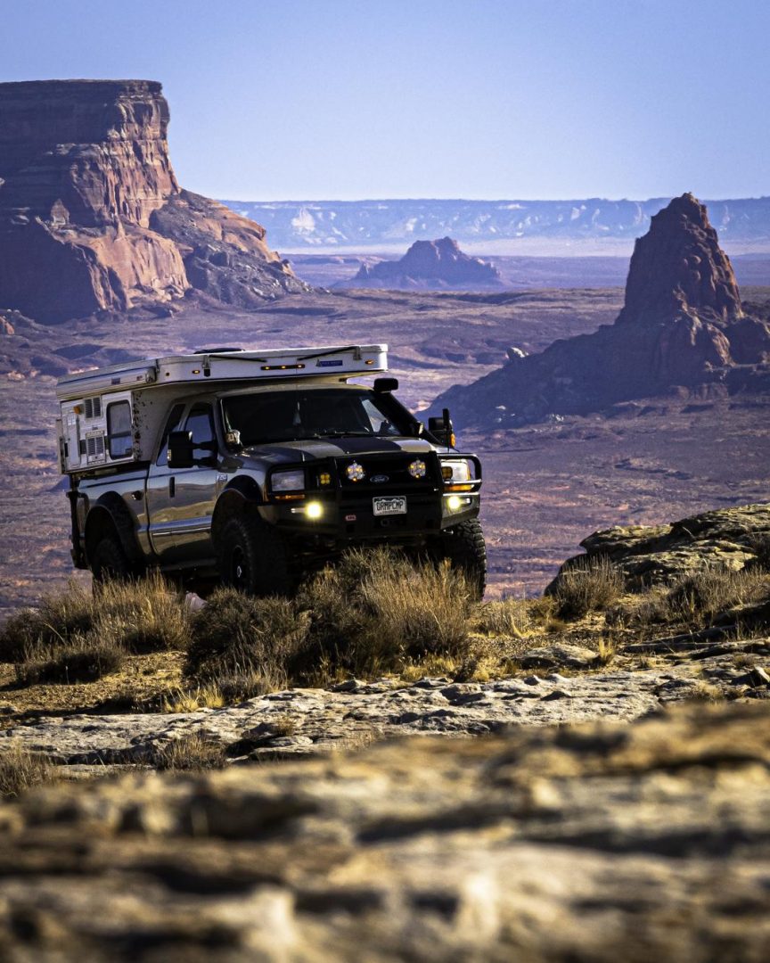 A landscape of Utah and a heavy duty truck with a pop-up camper attached. 