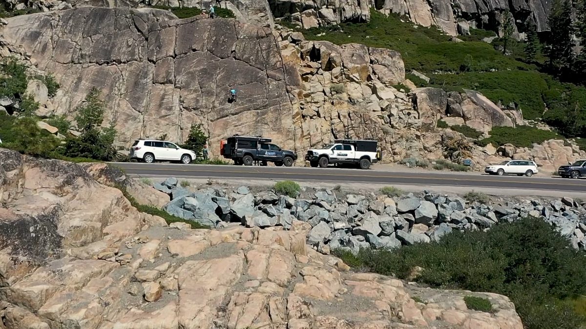 four wheel camper trucks parked next rock wall with mountain climbers climbing